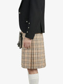 Person wearing a black blazer and beige plaid kilt on a white background