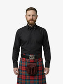 Man wearing a black shirt, bow tie, and red tartan kilt on a white background