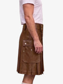 A side view of a person wearing a brown faux-leather kilt with pleated detailing and a large front flap pocket, paired with a white t-shirt against a plain white background.
