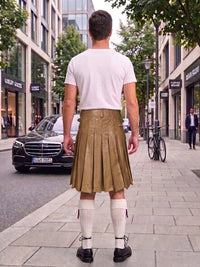 A man standing on a city sidewalk, viewed from behind, wearing a white t-shirt, a brown pleated leather kilt, white knee-high socks, and black shoes. Buildings, trees, a black Mercedes-Benz car, and a bicycle are visible in the background.