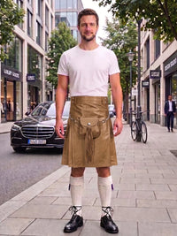 A man stands on a city sidewalk wearing a tan leather kilt with a front pouch and tie, paired with a white t-shirt, white knee-high socks, and black leather shoes. A black Mercedes-Benz is parked behind him on the street, with storefronts and trees in the background.