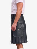 A man wearing a black faux-leather kilt with pleated detailing and front cargo pockets, paired with a white t-shirt, shown from a side profile against a light gray background.
