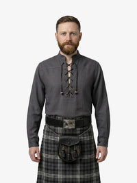 Man wearing a dark gray shirt with lace-up front and a plaid kilt on a white background