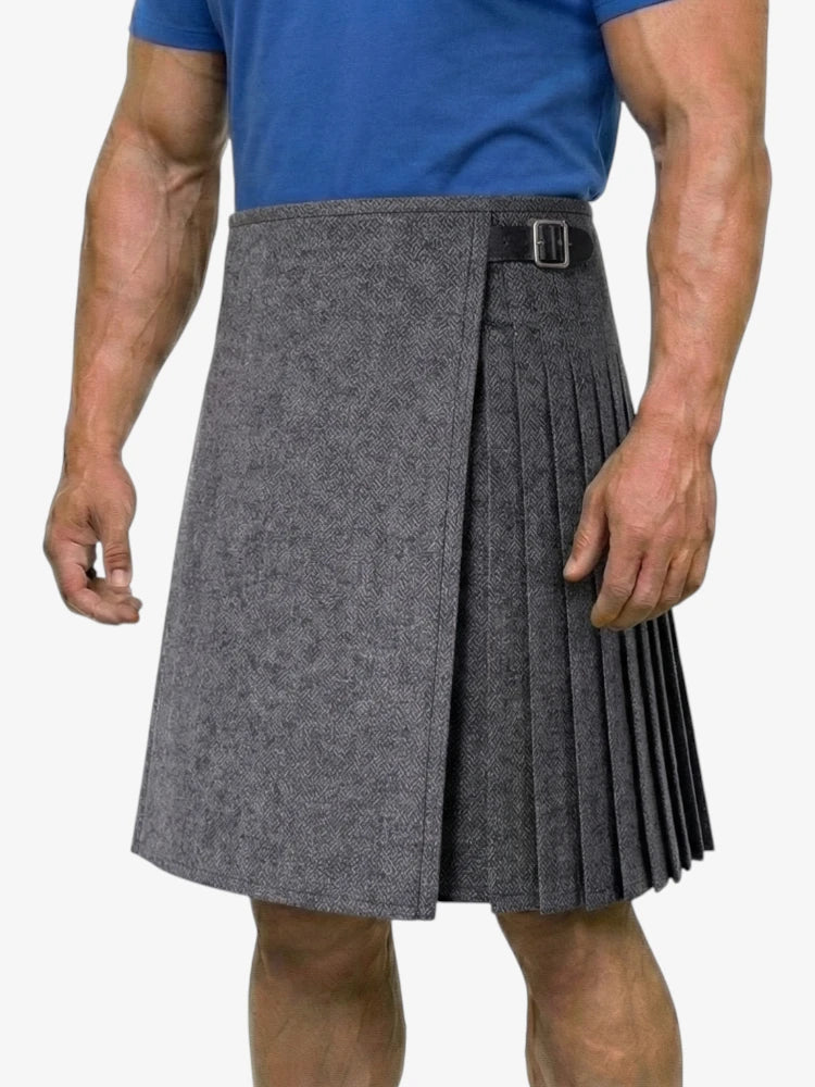 Person wearing a gray pleated kilt with a blue shirt on a white background