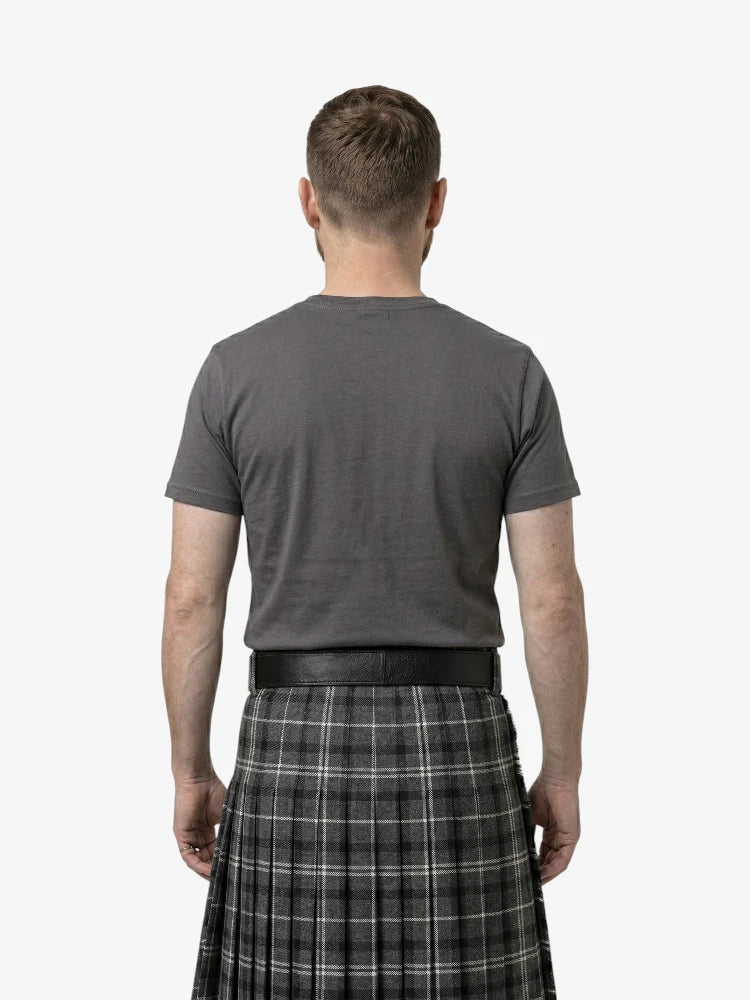 Man wearing a gray t-shirt and plaid kilt on a white background