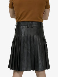 Person wearing a brown top and black pleated leather skirt on a white background