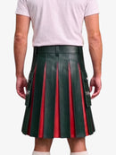 A person shown from the back wearing a dark green pleated leather kilt with red vertical stripe accents and silver hardware, paired with a light pink t-shirt and white socks, against a plain light gray background.