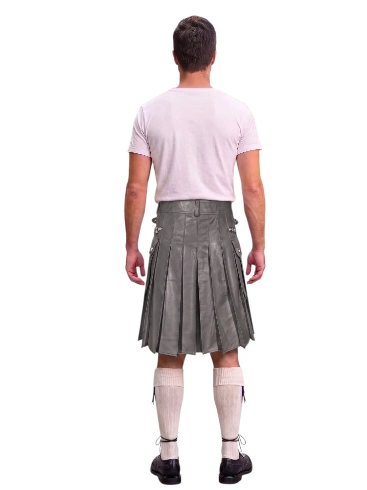 A man shown from the back wearing a gray pleated kilt, a light pink t-shirt, white knee-high socks, and black shoes, against a plain white background.