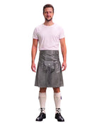 A man modeling a gray faux-leather kilt with a matching belt and pouch, paired with a white t-shirt, cream knee-high socks, and black lace-up shoes, against a plain white background.
