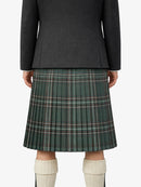 Person wearing a dark gray jacket and green plaid kilt on a white background