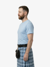 Man wearing a light blue t-shirt and plaid kilt on a white background