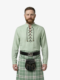 Man wearing a light green shirt with lace-up front and a green plaid kilt on a white background