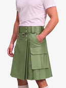 A person wearing a light sage green faux-leather kilt with a matching belt, silver-tone hardware, and cargo pockets, paired with a light pink t-shirt against a white background.
