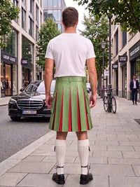 A man viewed from behind wearing a light green pleated kilt with red vertical stripes, a white t-shirt, white knee-high socks, and black shoes, standing on a city sidewalk.