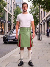 A man stands on a city sidewalk wearing a light green kilt with red side panels, a white t-shirt, white knee-high socks, and black shoes. Buildings, trees, a parked black car, and a bicycle are visible in the background.