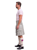 A man shown in profile wearing a light gray pleated kilt, a white t-shirt, white socks with a purple accent, and black shoes, against a plain white background.
