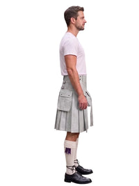A man shown in profile wearing a light gray pleated kilt, a white t-shirt, white socks with a purple accent, and black leather shoes, set against a plain white background.