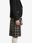 Person wearing a black blazer with silver buttons and a plaid kilt on a white background