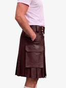 A dark green faux-leather kilt with pleated detailing, a front flap pocket, and a belt with silver-tone buttons, shown on a model wearing a light pink t-shirt against a white background.