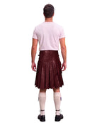 A man shown from the back wearing a dark brown leather kilt, a light pink t-shirt, cream-colored knee-high socks, and black shoes, against a solid white background.