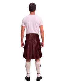 A man shown from the back wearing a dark brown leather kilt, a light pink t-shirt, cream-colored knee-high socks, and black shoes, against a solid white background.