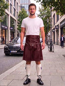 A man stands on a city sidewalk wearing a white crew-neck t-shirt and a dark brown leather kilt with a front pouch and strap details, paired with white knee-high socks and black leather shoes.
