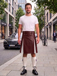 A man stands on a city sidewalk wearing a white crew-neck t-shirt and a dark brown leather kilt with white side panels, paired with white knee-high socks and black leather shoes.