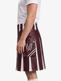 A person wearing a dark burgundy faux-leather kilt with bold white vertical stripes and silver-tone hardware, paired with a white t-shirt against a light gray background.