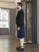 Man wearing a dark suit and blue plaid kilt in an elegant interior setting.