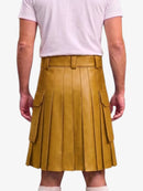 A mustard yellow pleated faux-leather kilt with side cargo pockets, shown on a model from the back wearing a light pink t-shirt and white socks against a light gray background.