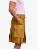 A mustard yellow faux-leather kilt with pleated detailing, a matching belt, and a large front flap pocket, shown on a model wearing a light pink t-shirt against a white background.