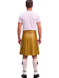 A man shown from the back wearing a mustard yellow leather kilt, a light pink t-shirt, white knee-high socks, and black shoes, isolated on a white background.