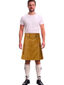 A man modeling a mustard yellow leather kilt with silver metal hardware, paired with a white t-shirt, white knee-high socks, and black lace-up shoes, against a plain white background.