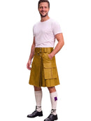 A man modeling a mustard yellow faux-leather kilt with a matching belt and metal hardware, paired with a white t-shirt, white knee-high socks, and black shoes, on a solid white background.