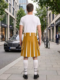 A man stands on a city sidewalk facing away from the camera, wearing a white short-sleeve T-shirt and a mustard yellow pleated kilt-style skirt with white vertical stripe panels, white knee-high socks, and black shoes. Storefronts, trees, a black car, and a bicycle are visible in the urban background.