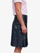 A side view of a person wearing a black leather pleated kilt with brass button details, paired with a white t-shirt, against a plain white background.
