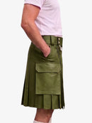 An olive green faux-leather kilt with pleated detailing, a belt, and a large front flap pocket, shown on a model wearing a light pink t-shirt against a white background.
