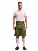 A man modeling a green faux-leather kilt with a front pouch and silver buckle, paired with a white t-shirt, cream knee-high socks, and black lace-up shoes, against a plain white background.