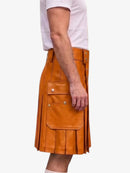 A side view of a person wearing a tan leather kilt with pleats and flap pockets, paired with a white t-shirt, against a plain light gray background.