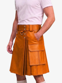 A person wearing a tan-brown leather kilt with a matching belt, silver-tone hardware, and large front cargo pockets, paired with a light pink t-shirt and white socks against a plain light gray background.