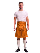 A man modeling a bright orange leather kilt with a front pouch and tassel detail, paired with a white t-shirt, cream knee-high socks, and black lace-up shoes, against a plain white background.