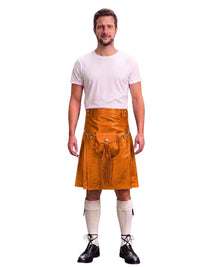 A man modeling a bright orange leather kilt with a front pouch and tassel detail, paired with a white t-shirt, cream knee-high socks, and black lace-up shoes, against a plain white background.