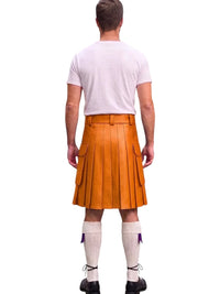 A man viewed from behind wearing a bright orange leather kilt, a light pink t-shirt, white knee-high socks, and black shoes against a plain white background.