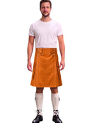A man modeling a mustard brown leather kilt with silver metal rivets and straps, paired with a white t-shirt, cream knee-high socks, and black lace-up boots, against a plain white background.