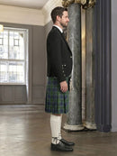 Man wearing a black jacket and green plaid kilt in an elegant interior setting.