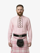 Man wearing a pink shirt with lace-up front and a pink plaid kilt on a white background