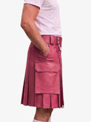 A person wearing a pink pleated leather kilt with a belt and large front flap pocket, paired with a light pink t-shirt, shown from the side against a plain light background.