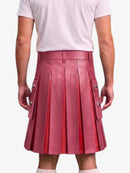 A person shown from the back wearing a pleated leather kilt in a dusty rose pink color, paired with a light pink t-shirt and white socks, against a plain light gray background.