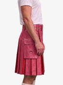 A model wearing a pink faux-leather kilt with pleated detailing, utility pockets, and a matching belt, paired with a white t-shirt against a light gray background.
