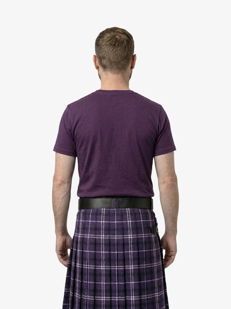 Man wearing a purple t-shirt and plaid kilt on a white background